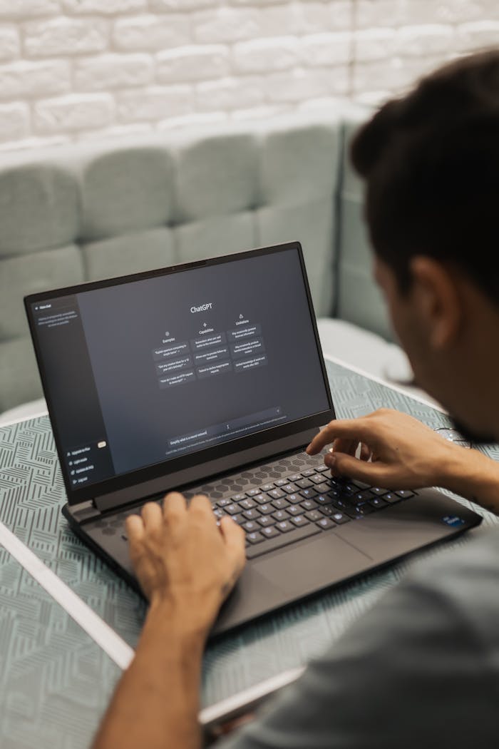team-02 A man types on a laptop running AI software, seated in a modern indoor setting.