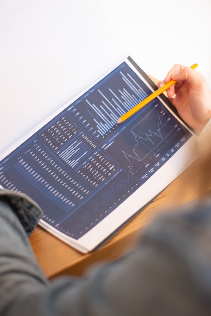 who-we-are A close-up of a person analyzing blue graph data with a yellow pencil.