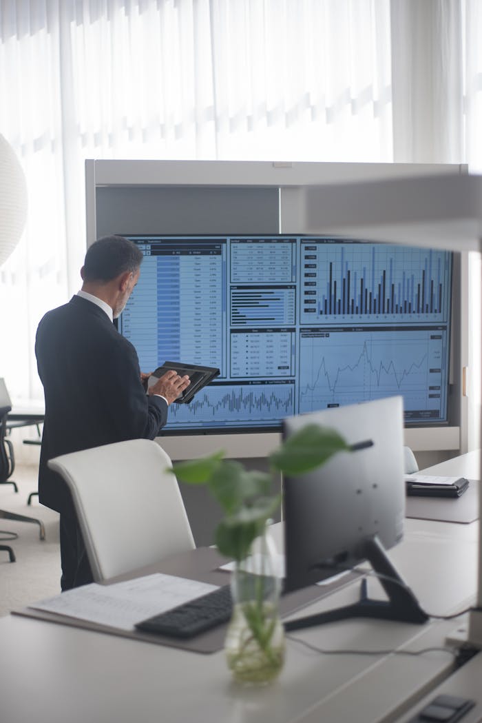 who-we-are A businessman in a modern office reviews data charts on a large screen with a tablet.