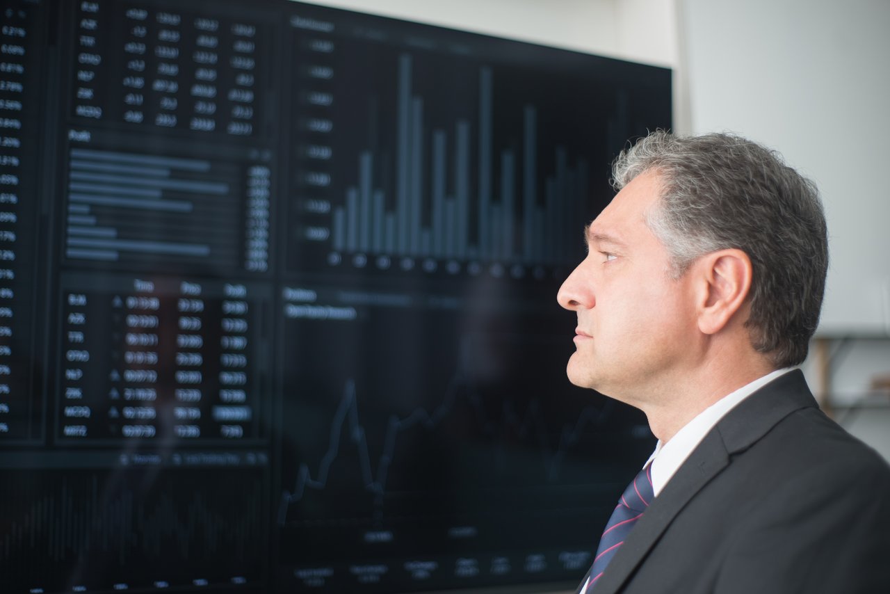 services-01 Mature businessman in corporate attire analyzing financial charts on a screen indoors.